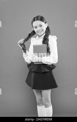 Lesen Lektion. Book Store Konzept. kleine Mädchen in Schuluniform. Angaben form Buch erhalten. Schulmädchen Notizen auf orange Hintergrund. zurück zu Schule. glückliches Kind. Zuversichtlich in ihr Wissen. Stockfoto