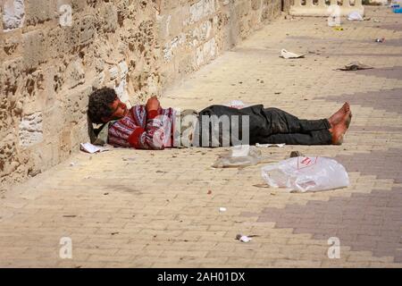 Ein obdachloser barfuß Mann, der auf der Straße zwischen dem Müll in Monastir, Tunesien liegt Stockfoto