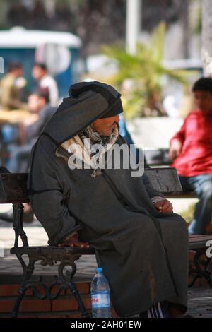 Ein alter tunesischer Mann in traditioneller Robe sitzt auf einer Bank auf dem Platz in Sousse, Tunesien Stockfoto