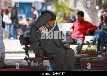 Ein alter tunesischer Mann in traditioneller Robe sitzt auf einer Bank auf dem Platz in Sousse, Tunesien Stockfoto