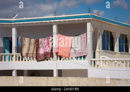 Bunte Bettwäsche und eine Bettdecke trocknen auf dem Balkon des Hauses in der starken Morgensonne in Hergla, Tunesien Stockfoto