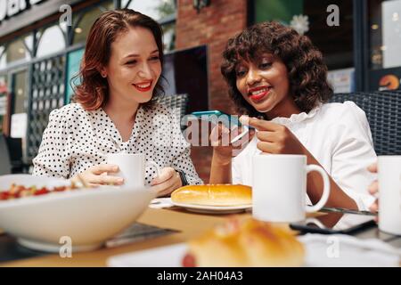 Fröhliche multi-ethnischen weibliche Freunde fotografieren Essen beim Mittagessen im Cafe zusammen Stockfoto