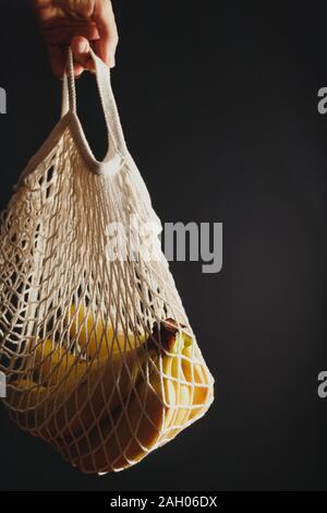 Hand hält eine Eco net Tasche mit Banane Zweig auf schwarzem Hintergrund. Stockfoto