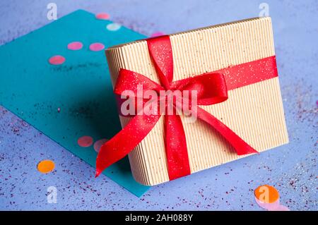 Nahaufnahme von Geschenkset mit leuchtend roten Farbband auf lila Hintergrund mit sparklets und Konfetti gebunden. Stockfoto