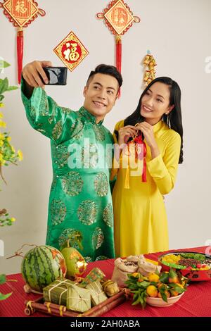 Schöne junge asiatische Paar in traditionellen Kostümen unter selfie bei TET-Fest Stockfoto