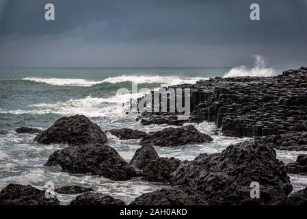 Meer Wellen schlagen die natürliche sechseckige Steine an der Küste namens Giant's Causeway, ein Wahrzeichen in Nordirland. Stockfoto