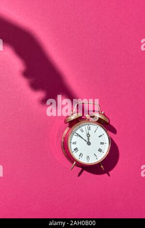 Harte Schatten aus der Hand des Weiblichen drückt auf altmodische Cooper malte Wecker auf einem rosa Hintergrund mit kopieren. Stockfoto