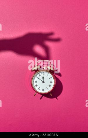 Retro Wecker lackiert Golden mit harten Schatten von Woman's Hand halten Sie den auf einem rosa Hintergrund, kopieren. Stockfoto