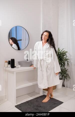 Hübsche Junge lächelnd brünette Frau im weißen Bademantel stehen auf kleine Wolldecke Stockfoto