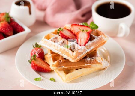 Belgische Waffeln mit Erdbeeren und Tasse schwarzen Kaffee auf einem rosa Hintergrund. Schmackhaftes süßes Frühstück essen. Reich an Zucker und Kohlenhydrate essen, ungesunde ea Stockfoto