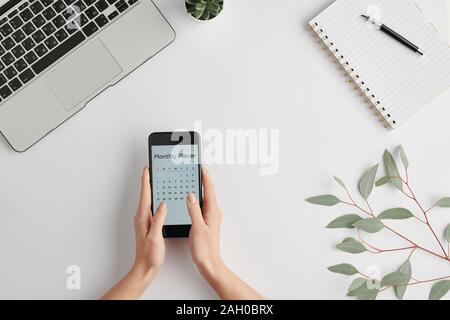 Hände von weiblichen Angestellten smartphone Holding mit monatlichen Planer auf dem Bildschirm Stockfoto