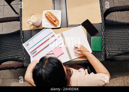 Frau sitzt im Cafe Tabelle mit Flugtickets und Planung Reise bei Kaffee und Würstchen zum Frühstück Stockfoto