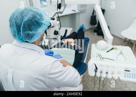 Arzt Mikroskop. Zahnarzt ist die Behandlung von Patienten in der modernen zahnmedizinischen Büro. Die Bedienung erfolgt mittels Fangdamms durchgeführt. Client wird eingefügt und wiederhergestellt Stockfoto