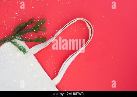 Canvas Baumwolle weiß Tasche und Zweig der Weihnachtsbaum auf hellen roten Hintergrund. Umweltfreundliche, wiederverwendbare Tasche zum Einkaufen. Eco und null Abfall Konzept. Stockfoto