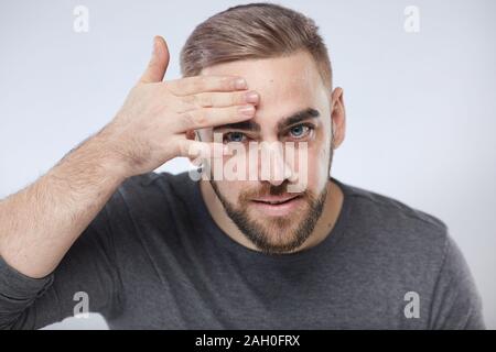 Kopf und Schultern studio Portraitfotos der überzeugten Mann Anwendung feuchtigkeitsspendende Gesichtscreme auf seinem Gesicht, weißer Hintergrund Stockfoto