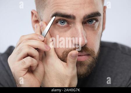 Horizontale Nahaufnahme Portrait von gutaussehenden jungen Mann tweezing seine Augenbrauen an Kamera suchen Stockfoto