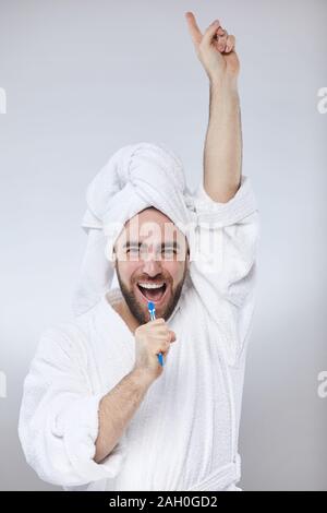 Vertikale studio Portrait der kaukasischen Mann tragen weiße batrhrobe und Handtuch turban Spaß singen Songs in den Zahnbürste Stockfoto