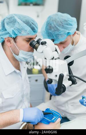 Arzt Mikroskop. Zahnarzt ist die Behandlung von Patienten in der modernen zahnmedizinischen Büro. Die Bedienung erfolgt mittels Fangdamms durchgeführt. Client wird eingefügt und wiederhergestellt Stockfoto