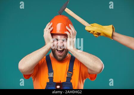 Konzeptionelle studio Portraitfotos der Bauarbeiter tragen, hardhat, Hammer in seinem Kopf schlagen und Schmerzen Stockfoto