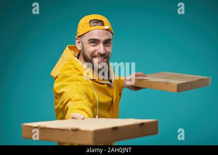 Taille bis horizontale Portrait von jungen erwachsenen Mann mit leuchtend gelben Uniform liefern Pizza, Türkis Hintergrund Stockfoto