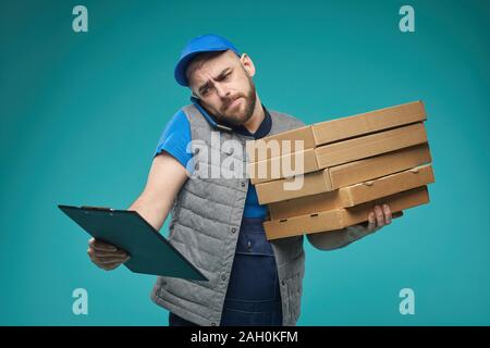 Horizontale medium Studio Aufnahme von Nahrung boten Holding Pizzakartons, am Telefon sprechen und die Überprüfung der Liste mit ernsten Gesichtsausdruck Stockfoto