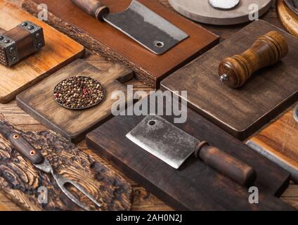 Verschiedene Größen und Formen Küche Schneidebretter auf hölzernen Hintergrund mit Fleisch, Beile, Messer und Gabel und andere Utensilien. Stockfoto