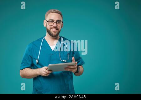 Horizontale medium Studio Portrait der Kaukasischen medizinischer Arbeiter tragen blaue Uniform holding Tablet-PC in die Kamera lächeln Stockfoto
