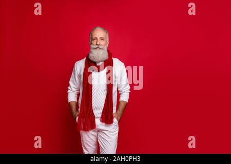 Trendy älterer Mann santa wie Stil, Hände in den Taschen tragen Sie warme Kleidung aus Gewirken isolierten roten Hintergrund Stockfoto