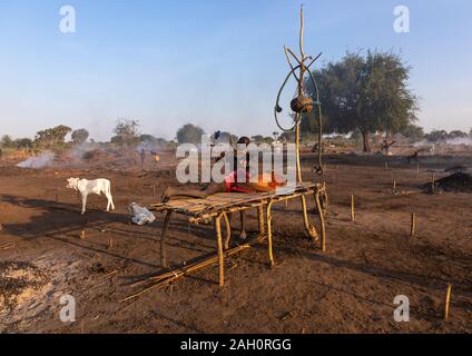 Mundari Stamm junge ruht auf einem Bett aus Holz in der Mitte seiner langen Hörner Kühe, Central Equatoria, Terekeka, South Sudan Stockfoto