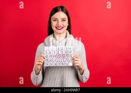 Hübsche Dame holding Papier Kalender in den Händen aufgeregt Ferienhäuser Verschleiß gestrickte Pullover isolierten roten Hintergrund zu erfüllen Stockfoto