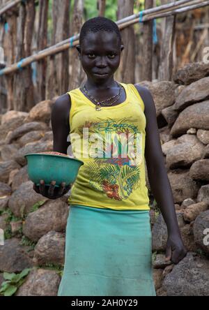 Lotuko Stamm Frau, die Essen vor einer Mauer aus Stein, Central Equatoria, Illeu, South Sudan Stockfoto