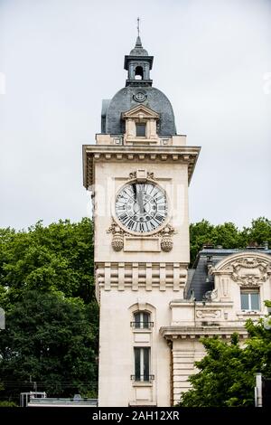 Kirchturm mit Uhr gegen Bäume und blauen Himmel im Hintergrund Stockfoto