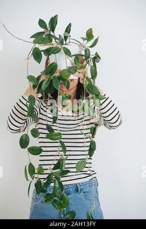 Frau, ihr Gesicht hinter einer Topfpflanze, sie halten. Über weiß. Stockfoto