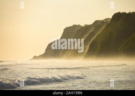 (Selektive Fokus) einen atemberaubenden Blick auf die Melasti Beach mit seinem Felsen durch eine raue Meer bei einem schönen Sonnenuntergang, South Bali, Indonesien getaucht. Stockfoto