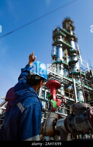 Arbeitnehmer in der blauen Uniform und dem blauen Helm und Grau destillationskolonne an der Ölraffinerie in den blauen Himmel. Stockfoto