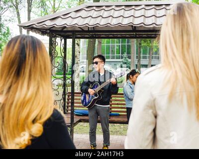 Bischkek, Kirgisistan - April 14, 2018 Zwei Mädchen hören, ein Musiker mit einer Gitarre auf der Straße Stockfoto