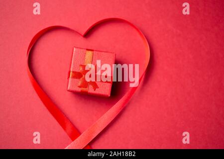 Roter Geschenkbox mit Herz aus roten Geschenk Bogen über den roten Hintergrund. Romantische greating Karte. Stockfoto
