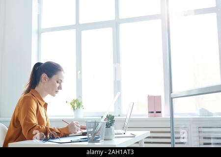 Junge ernsthafte Manager sitzen an ihrem Arbeitsplatz vor dem Laptop und Schreiben in Dokumenten Sie arbeiten mit dem im Büro Stockfoto