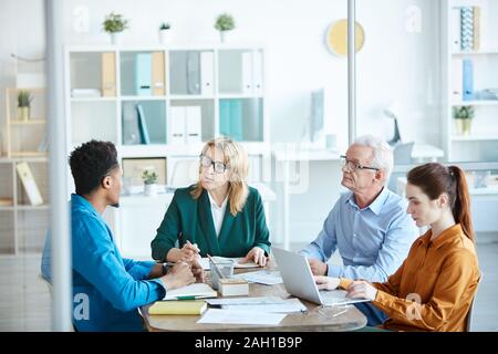 Reife weibliche Führer im Gespräch mit Ihren Mitarbeitern und Ihnen einige Anweisung, während Sie am Tisch sitzen während der Sitzung Stockfoto