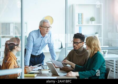 Reifen Geschäftsmann in Brillen und Erläuterung der Business Strategie für junge Geschäftsleute am Tisch in der Sitzung im Büro Stockfoto