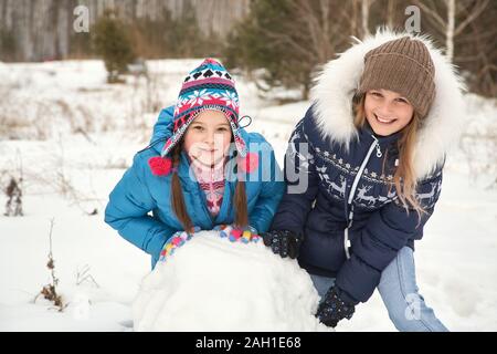 Zwei Freundinnen bauen einen Schneemann. Lustige Mädchen auf einem Spaziergang im Winter im Freien. Stockfoto