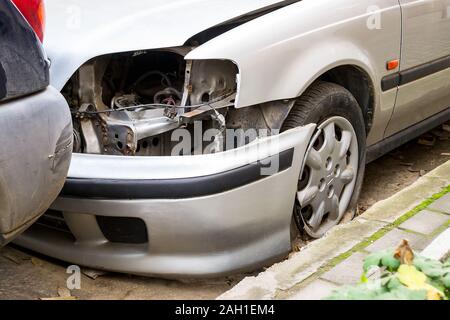 Stationäre silver Auto ohne Scheinwerfer und mit einem abgefallen Stoßfänger an den Bürgersteig gefärbt. Folgen von Unfall oder Vandalismus. Low Angle View. Stockfoto