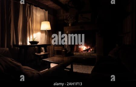 Innenraum eines Holz- und gemütliches Blockhaus mit bequemen Sofas, Land, Dekoration, schwach beleuchtet durch den Kamin und eine Lampe. Konzept der Stille Stockfoto