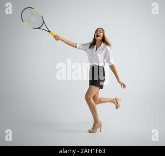 Wenn es Sie nach oben. Frau im Amt Kleidung Tennis spielen auf Grau studio Hintergrund. Geschäftsfrau Training in Bewegung, Aktion. Ungewöhnlichen Blick für Sport, neue Aktivität. Sport, gesunde Lebensweise. Stockfoto