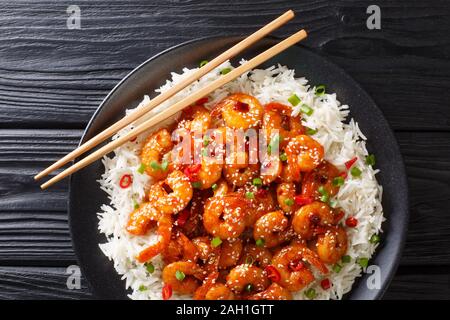 Klebrige gebratene Garnelen mit Knoblauch, Chilli, Sesam und grüne Zwiebeln mit Reis in der Nähe serviert in einem Teller auf dem Tisch. horizontal oben Blick von abov Stockfoto