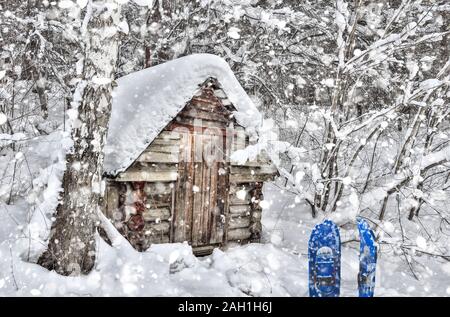 Kleine alte Holzhütte in der Nähe von Birken in verschneite sibirische Winter Forest bei starker Schneefall. Blau Schneeschuhwandern im Schneetreiben in der Nähe der Tür. Märchen Stockfoto