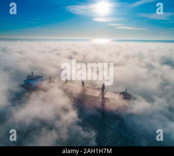 Frachtschiff und Krane Silhouetten in Meer Nebel, Kran Schiff arbeiten für die Lieferung von Containern. Stockfoto