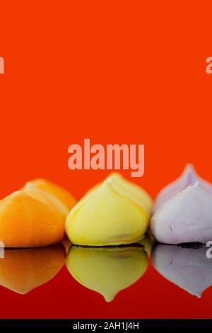 Baisers, verschiedene Farben, auf orangem Hintergrund reflektiert. Auf einer glänzenden Oberfläche. Stockfoto