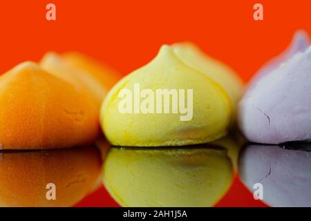 Baisers, verschiedene Farben, auf orangem Hintergrund reflektiert. Auf einer glänzenden Oberfläche. Stockfoto