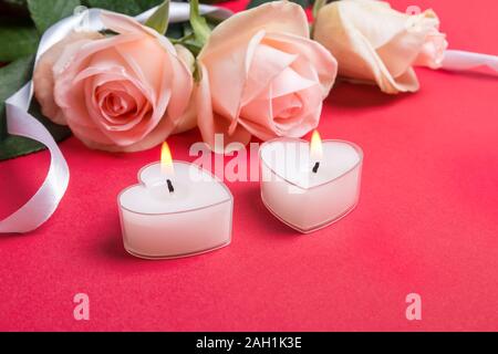 Zwei Kerzen in Herzform und sanften Pastelltönen Rosen auf roten Hintergrund. Valentinstag Zusammensetzung Stockfoto